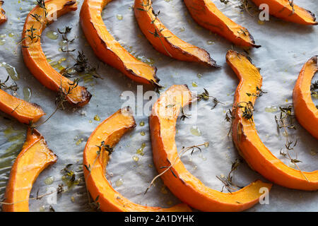 Petites Tranches de rôti au thym de citrouille, l'huile d'olive et de sel sur du papier sulfurisé et lèchefrite. Vegan délicieux en-cas. Patern alimentaire. Banque D'Images