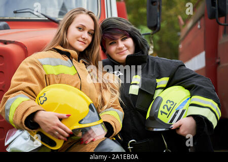 Photo de deux femmes pompier avec casque dans ses mains se tenait à côté de la voiture de pompiers sur la rue Banque D'Images