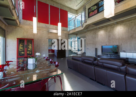 Intérieur de maison moderne, salle à manger avec table en verre et chaises, méthacrylate rouge hauteur double. Banque D'Images