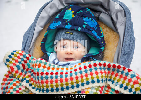 Un petit garçon de race blanche âgés entre 4 et 5 mois aux yeux bleus dans une poussette en hiver couverte par une couverture crochetée portant un chapeau en laine Banque D'Images