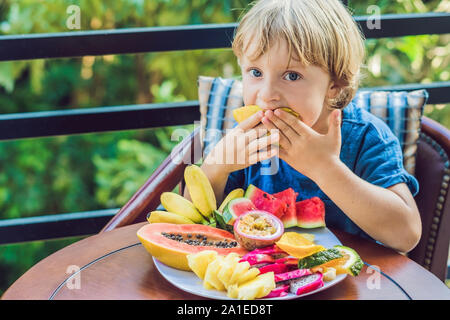 Le garçon est en train de manger fruits différents sur la terrasse. Banque D'Images