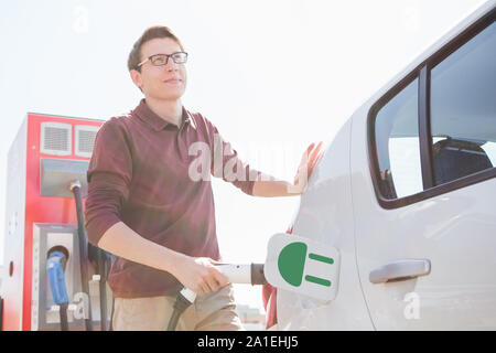 L'homme est debout près de la voiture électrique. La voiture est en charge à la station de charge pour les véhicules électriques. Banque D'Images