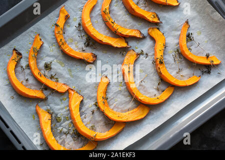 Petites Tranches de rôti au thym de citrouille, l'huile d'olive et de sel sur du papier sulfurisé et lèchefrite. Vegan délicieux en-cas. Patern alimentaire. Vue de dessus. Banque D'Images