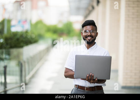 Indien de l'American College Student est assis sur des escaliers sur le campus, travaille sur un ordinateur portable. Banque D'Images