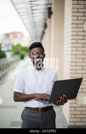 Indien de l'American College Student est assis sur des escaliers sur le campus, travaille sur un ordinateur portable. Banque D'Images