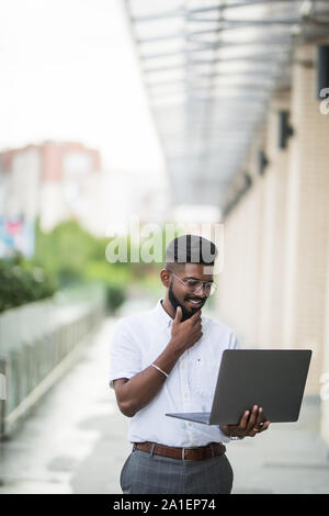 Indien de l'American College Student est assis sur des escaliers sur le campus, travaille sur un ordinateur portable. Banque D'Images