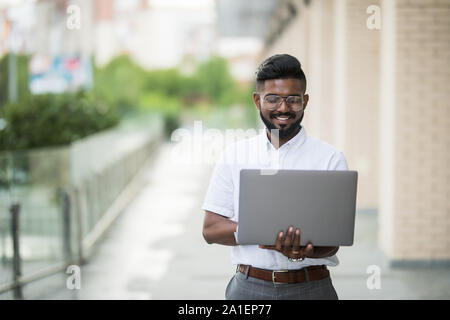 Indien de l'American College Student est assis sur des escaliers sur le campus, travaille sur un ordinateur portable. Banque D'Images