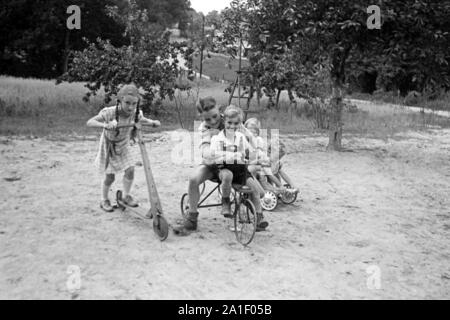 Kinder spielen mit und Rouleau Dreirad auf einem Spielplatz, Deutschland 1939. Les enfants avec des tricycles et scooters sur une aire de jeux, Allemagne 1939. Banque D'Images