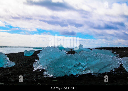 Banc de glace sur une plage de sable noir avec vue sur la mer et ciel nuageux en arrière-plan. Photographié dans la lagune de Jökulsarlon dans le sud de l'Islande Banque D'Images