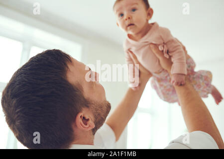 Jeune père aimant debout dans son salon à la maison en tenant son bébé adorable girl joyeusement en l'air Banque D'Images