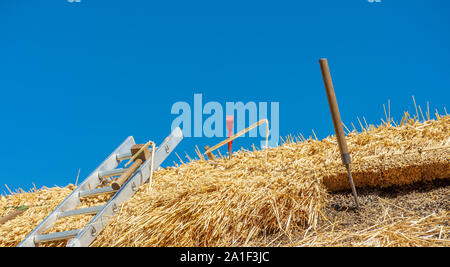 Outils sur le toit d'un village de chaume chalet comme il est en cours de réparation et de renouvellement Banque D'Images