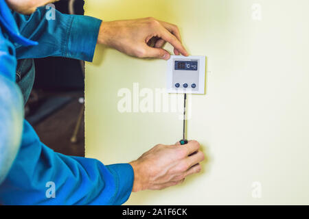 Electricien installation d'un thermostat électrique dans une maison neuve. Banque D'Images