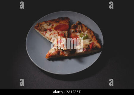 Deux tranches de pizza chaude sur bleu-gris soucoupe sur fond sombre Banque D'Images