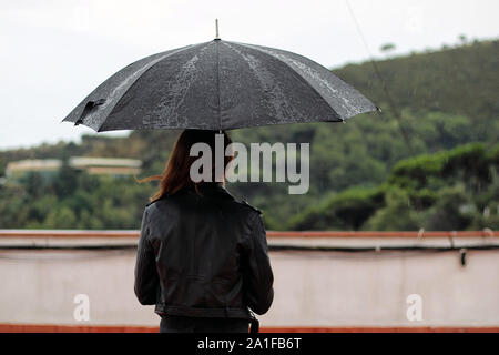 Jeune femme avec un manteau de cuir tient ouverte parapluie noir dans sa main sous la pluie. Le garçon se trouve derrière la montagne. Banque D'Images