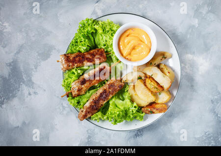 Shish kebab grillé servi avec pommes frites et sauce sur fond de béton. Vue d'en haut Banque D'Images