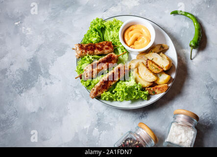 Shish kebab grillé servi avec pommes frites et sauce sur fond de béton. Copy space Banque D'Images