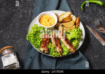 Shish kebab grillé servi avec pommes frites et sauce sur fond noir en noir Banque D'Images