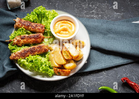 Shish kebab grillé servi avec pommes frites et sauce sur fond noir en noir Banque D'Images