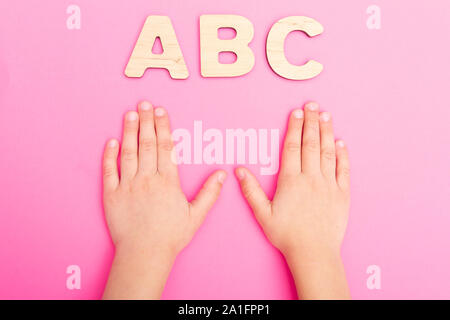 ABC des lettres dans les mains de l'enfant sur fond rose. Banque D'Images