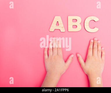 ABC lettres avec les mains de l'enfant sur fond rose. Banque D'Images