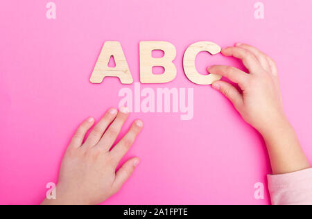 ABC des lettres dans les mains de l'enfant sur fond rose. Banque D'Images