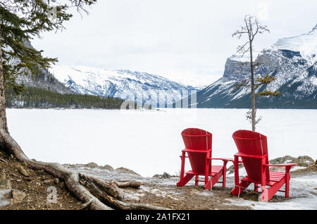 Chaises rouge vide face à un beau lac gelé sur une journée d'hiver. Le parc national Banff, AB, Canada. Banque D'Images