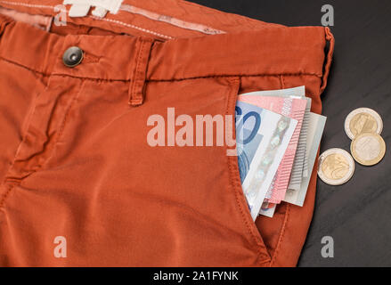 Euro Monnaie de papier collage hors de la poche de son pantalon et pièces jeter sur une table en bois noir Banque D'Images