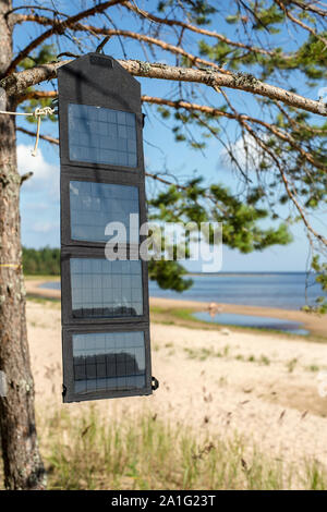 Panneau solaire pliable portable accroché sur la batterie à l'extérieur, sur un pin au bord de la mer près de la plage de sable Banque D'Images