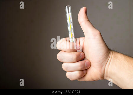 Un homme malade de la tenue d'un thermomètre médical et showing thumb indiquant qu'il est très bien Banque D'Images