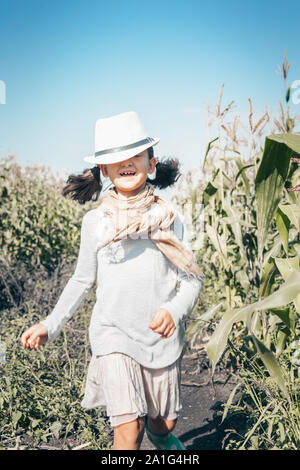 Happy little girl qui traverse un champ. Heureux enfant de sexe féminin dans les tenues de l'extérieur. Smiling kid dans le village. Fille avec le visage satisfait expressio Banque D'Images