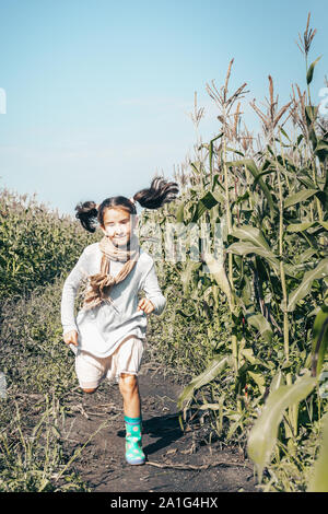 Happy little girl qui traverse un champ. Heureux enfant de sexe féminin dans les tenues de l'extérieur. Smiling kid dans le village. Fille avec le visage satisfait expressio Banque D'Images