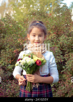 De graves little girl holding bouquet fleurs et feuilles. Enfant, en uniforme d'outdoor. Portrait d'écolière. Fille avec une expression faciale. Banque D'Images