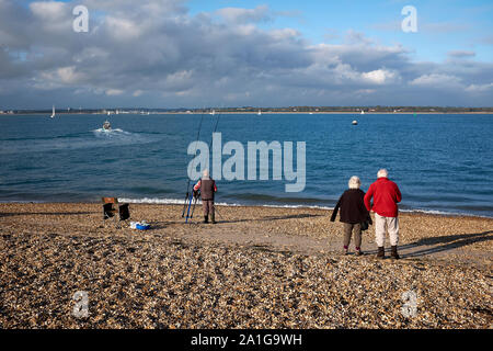 Deux personnes regardant un bateau se déplaçant le long de la Solent dans la Manche, à partir de la plage de Calshot UK alors qu'un pêcheur met en place des prêts pour une journée de pêche Banque D'Images