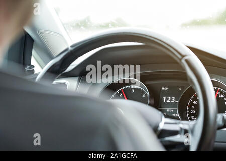 L'homme conduisant une voiture, vue à partir de la banquette arrière, détail sur planche de bord et le volant Banque D'Images