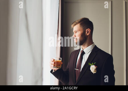 Portrait d'un jeune homme barbu avec look rétro tenant un verre de whisky sur fond gris Banque D'Images