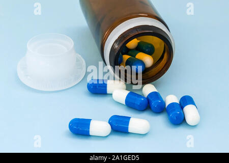 Close-up of pills dispersés de pot en verre brun sur un fond bleu. Capsules bleu blanc renversé sur un verre bouteille de pilules. À être malade, prendre des pilules Banque D'Images