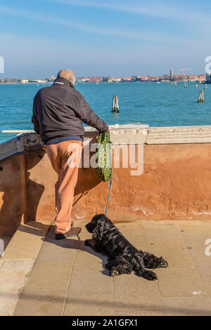 Venise, Italie - 01 NOVEMBRE 2014 : un homme avec un chien noir sur le bord de l'eau se penche sur la distance entre le détroit de l'île Banque D'Images