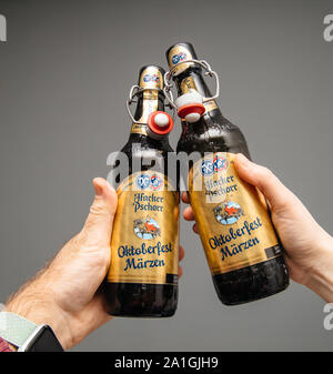 Munich, Allemagne - 3 Mar 2019 : Close-up of man and woman hand holding boire bouteille de bière traditionnelle Marzen Comprimés Hacker Pschorr beer contre l'arrière-plan gris Banque D'Images