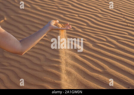 Le sable glisser entre les doigts d'une main de femme dans le désert. Banque D'Images