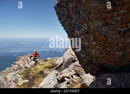 Athlète coureur avec barbe en chemise orange fonctionnant sur le sentier dans les montagnes Banque D'Images