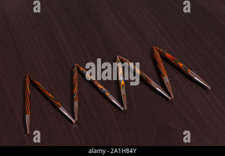 Les aiguilles à tricoter en bambou multicolores de tailles différentes, disposés dans une rangée sur une table en bois sombre, vue du dessus Banque D'Images