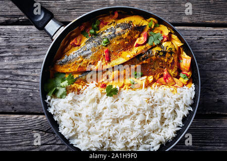Close-up of Yellow curry, curry Panang avec Saba maquereau grillé poisson servi avec riz long grain cuit à la vapeur dans une poêle sur une table en bois rustique, vue Banque D'Images