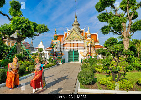 En face des deux géants de Yak (temple guardian) statues, deux touristes posent en tenue traditionnelle thaïlandaise embauché ; Wat Arun (Temple de l'aube), Bangkok, Thaïlande Banque D'Images