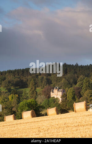 Vue de ballots de paille dans un champ de chaume, avec Craigievar Castle sur une colline boisée à l'arrière-plan Banque D'Images