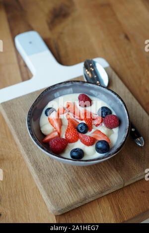 Petits fruits et crème dessert dans une profonde cuvette d'argile servi sur planche de bois Banque D'Images