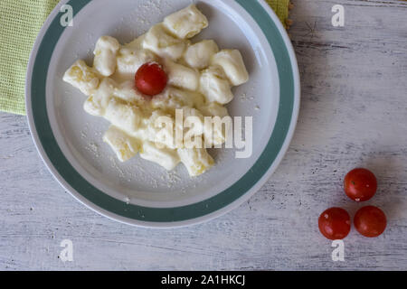 Plaque blanche de gnocchi de pommes de terre crémeux chaud servi avec des tomates cerises/ couverts/ contexte alimentaire - Image Banque D'Images