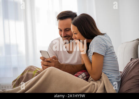 Young happy couple looking at smartphone est au lit le matin. Banque D'Images