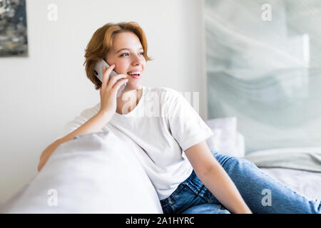 Smiling woman sitting on sofa dans le salon ayant un appel téléphonique. Banque D'Images