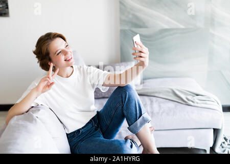 Belle brune assise sur son canapé en prenant une photo d'elle-même à la maison dans le salon Banque D'Images