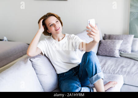 Belle brune assise sur son canapé en prenant une photo d'elle-même à la maison dans le salon Banque D'Images